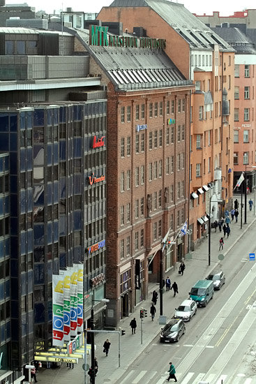 The view across the street to the nest-site. The three chicks can be seen in their nest on the roof terrace, where the near modern building meets the red brick building. The cropped version of the same image below shows them in more detail.